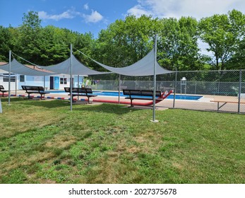 Tents And Benches Setup Outside Of A Public Pool. The Public Park Is Empty But The Community Area Is Fenced Off. There's A Tall Lifeguard Chair In The Center Of Pool For Someone To Keep Watch.