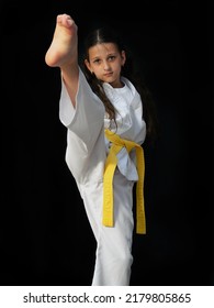 A Ten-year-old Girl Is Training Taekwondo. Female Child Makes A Kick On A Black Background