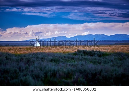 Tepee in open field with mountains in the background.