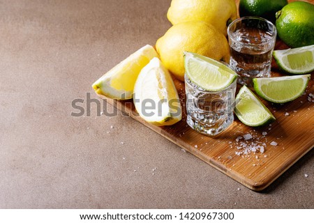 Tequila in a glass served with lemons, limes and salt over brown texture background
