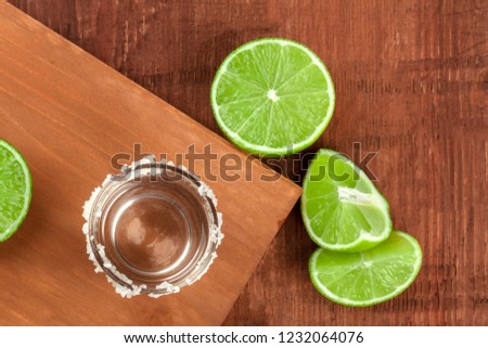A tequila shot with fresh lime wedges, shot from above on dark rustic textures with a place for text