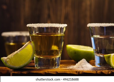Tequila shots, salt and lime slices over wooden background. Toned image. Selective focus - Shutterstock ID 496218688