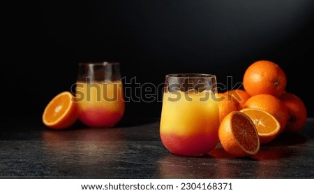Tequila sunrise cocktail with ice and grenadine on a black background.