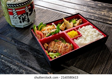 Teriyaki chicken bento with dumplings and salad in the traditional Japanese ramen restaurant, with bento box on and Japanese fonts sake barrel translation: Invincible Great Gate
