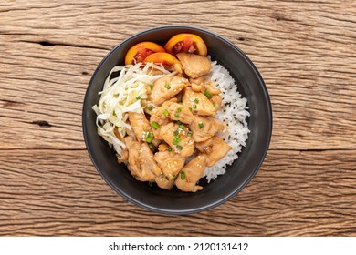 Teriyaki Chicken Donburi, Japanese food, streamed rice with Teriyaki chicken, mince cauliflower, tomato, spring onion and sesame in black ceramic bowl on rustic wood texture background, top view
