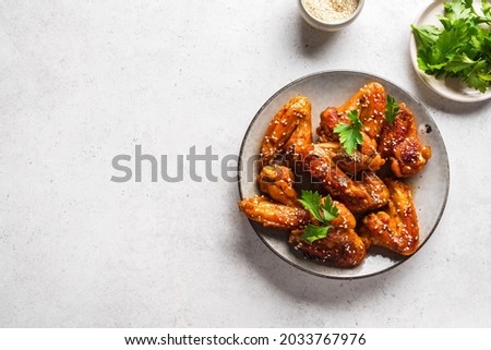 Teriyaki chicken wings with sesame and greens on white background, top view, copy space. Asian style meal - roasted chicken wings with teriyaki sauce.