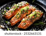 Teriyaki salmon filets sprinkled chopped scallion in a black baking dish, focus on the middle, close up view