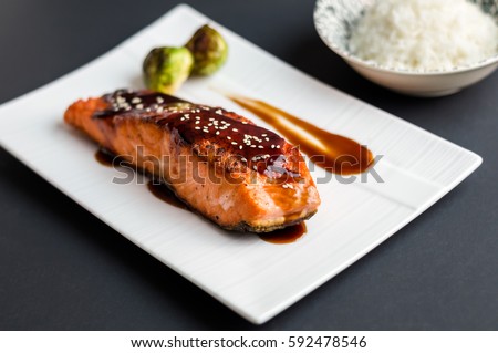 Teriyaki salmon on black background. Japanese cuisine inspired dinner consisting of grilled salmon fillet glazed in delicious teriyaki sauce (soy sauce base). Brussel sprouts and white rice as sides.
