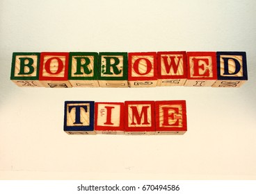 The term borrowed time visually displayed on a white background using colorful wooden blocks in landscape format with copy space