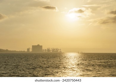 Terminal Portuario da Trafaria the port of Trafaria with cranes in the hazy distance during golden sunset, Lisbon, Portugal - Powered by Shutterstock