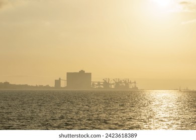 Terminal Portuario da Trafaria the port of Trafaria with cranes in the hazy distance during golden sunset, Lisbon, Portugal - Powered by Shutterstock