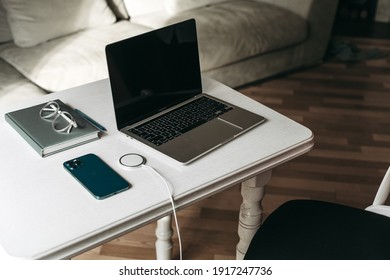 Ternopil, Ukraine - 01.31.2021:
Gray MacBook Pro 2020 Laptop On M1 Chip, Apple Iphone 12 Pro Max Blue Smartphone With Wireless Charging On A White Wooden Table In The Office With A Notebook, Glasses