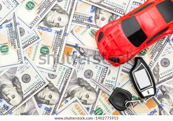 Ternopil, Ukraine - March 30, 2019: Remote control\
with car key and red car toy on background of dollar bills. Top\
view. Space for text.