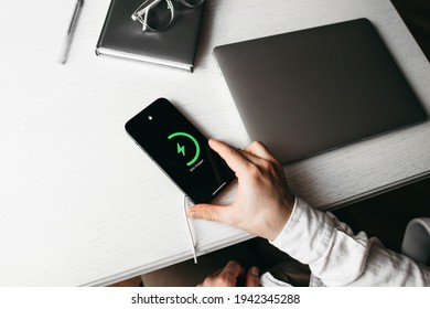 Ternopil, Ukraine-01.31.2021
The Man Is Charged Smartphone  Wireless On A White Wooden Table With Laptop At Office Place. New Technology, Apple Mobile Phone, Green Charging, IPhone 12 Pro Max