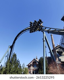 A terquoise rollercoaster passes through a zero G roll. Below is a 19th century house