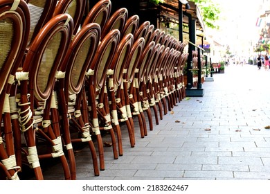 Terrace Chairs Stacked Along Walking Street In European Urban Downtown Area. Diminishing Perspective. Travel And Tourism Concept. Street Resaurant Patio. Rattan Garden Furniture.