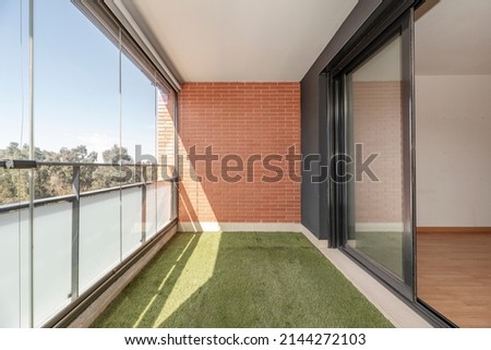 Terrace with glass wall, artificial grass floor and painted iron railing in urban residential house on a sunny spring day