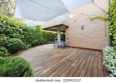 Terrace of a ground floor house with hedges and ornamental plants, slatted acacia hardwood floors twin wooden sunbeds and white awnings - Shutterstock ID 2255912157