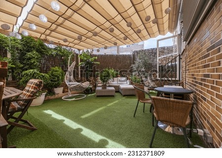Terrace of a house with artificial grass floors, tables, outdoor seating, lots of plants and an extended retractable awning
