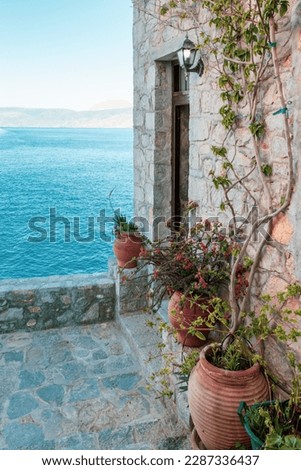 Terrace with outdoor decoration of terracotta pots against an ancient facade overlooking the Aegean Sea, Hydra Island, Greece.