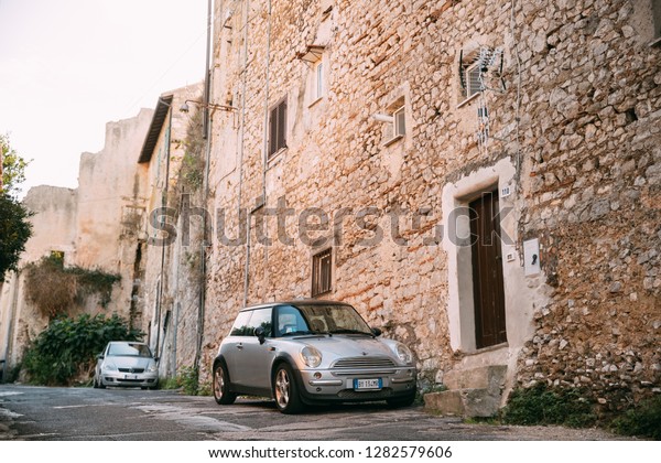 Terracina, Italy - October 15, 2018:\
Front View Of Gray Color 2004 Mini One Hatch (pre-facelift model)\
Mini Cooper Car Parking On Street Near Old Italian\
House.