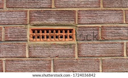 Terracotta coloured air brick embedded with a textured red brick wall.