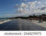 Terrazza con molti panelli solari che si affaccia su un panorama marino con molti alberi sotto un cielo azzurro denso di nuvole bianche.