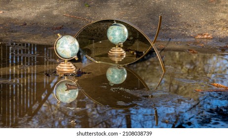 Terrestrial Globe Placed In A Puddle On The Ground, Mirror In The Background, Multiple Reflections