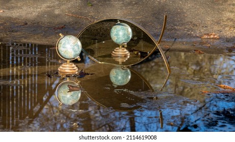 Terrestrial Globe Placed In A Puddle On The Ground, Mirror In The Background, Multiple Reflections