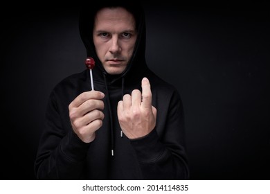 terrible threatening adult man in black wear offering candy lollipop to children standing on black studio background, portrait of caucasian maniac pedophile male looking at camera confidently