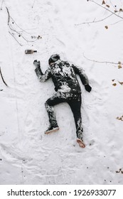 A terribly drunk homeless and dirty man in a black coat lies sleeping on his stomach on white snow in a frosty winter with a bottle of alcohol, strong whiskey. Photography, copy space, concept.