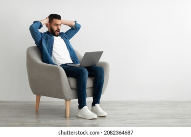 Terrified Arab Freelancer Looking At Laptop Screen, Grabbing His Head, Making Mistake In Business Project, Missing Deadline Against White Studio Wall, Copy Space. Young Man Having Online Work Stress