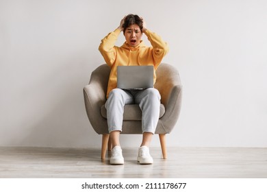 Terrified Asian male freelancer looking at laptop screen, grabbing head, making error in business project, missing deadline against white wall, full length. Young guy suffering from online work stress