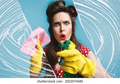 Terrified Pinup Woman In Retro Dress Cleaning Glass With Detergent And Rag, Wiping Soap Suds On Blue Studio Background. Classic Millennial Lady Doing Household Duties