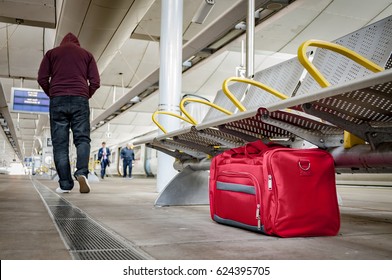 Terrorism And Public Safety Concept With An Unattended Bag Left Under Chair On Platform At Train Station Or Airport And Man Wearing A Hoodie Walking Away From The Suspicious Item (possibly Terrorist)