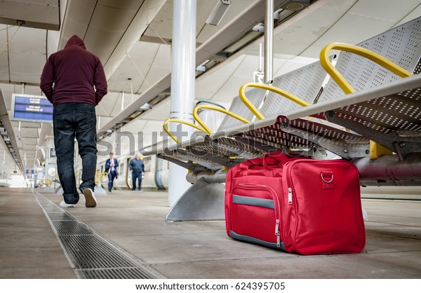 Terrorism and public safety concept with an\
unattended bag left under chair on platform at train station or\
airport and man wearing a hoodie walking away from the suspicious\
item (possibly\
terrorist)