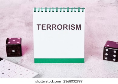 TERRORISM text on a white notepad sheet next to dice on an abstract background