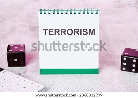 TERRORISM text on a white notepad sheet next to dice on an abstract background