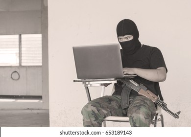 Terrorist In Black Mask With Gun And Working On His Computer.