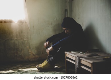 A terrorist looks so despair, depressed and sad. He wants suicide by using a bomb. Handsome man sits on a dark and dirty room.   A guy feels hopeless with sunlight through the window