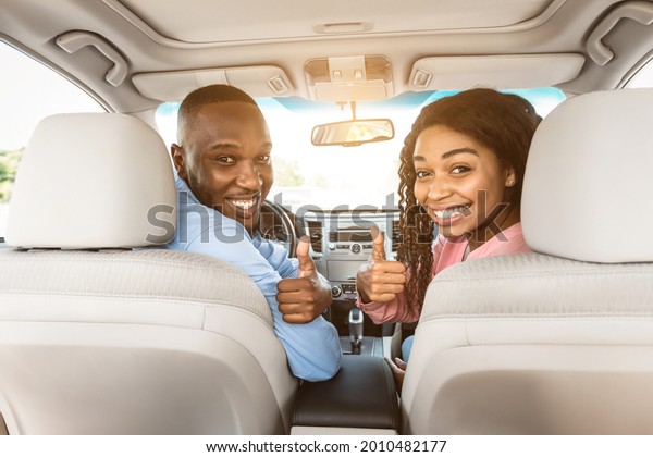 Test Drive, Great Ride, Good Car Concept. Portrait\
Of Excited African Amercan Couple Showing Thumbs Up Sign Gesture,\
Sitting On Front Seats In New Auto, Looking Vack At Camera Buying\
Vehicle In Store