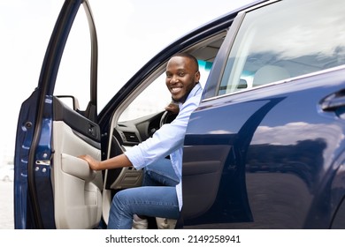 Test drive, Leasing, Buying, Rent Concept. Cheerful young African American guy going out or getting in the car, looking posing at camera. Happy black male open automobile door in the city outdoors