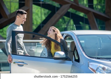 Test Drive. Young Pretty Woman Opening The Car Door And Talking To The Young Man