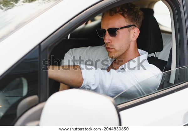Test driving of new generation\
electro vehicle with self driving system. Handsome Caucasian man\
sitting behind the wheel of new modern car and smiling at\
camera.
