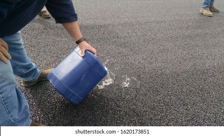 Test of pervious pavement demonstration with roadway water not puddling. Worker pouring water directly onto road. 