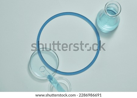 A test tube, glass petri dish and an erlenmeyer flask filled with blue fluid are arranged on white background. Empty area for product presentation