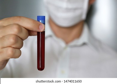 Test Tube In Male Hand Close Up, Man In Medical Mask Holding A Vial With Red Liquid. Concept Of Blood Sample, Medical And Chemical Research, Vaccination, Doctor Or Scientist