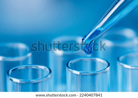 Test tubes with blue liquid water samples and pipette over blue background. Pipette dropping sample into test tube. Laboratory glassware, science laboratory research concept.