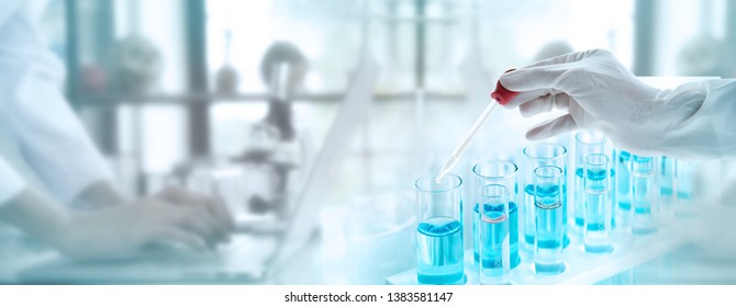 Test tubes with liquid in laboratory, Doctor hand holding dropper with dripping transparent glass pipette. scientist working with laptop background for banner size text space.
