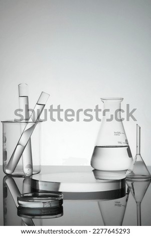 Test tubes, petri dish and erlenmeyer flask containing water, transparent podium in round shape with empty space for product presentation. Laboratory concept